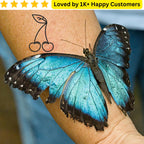 Blue butterfly on a person's arm with a tattoo of a cherry, set against a blurred background. Bold, Skin-Safe Tattoos for Women Who Love Fashion Without the Commitment&nbsp;