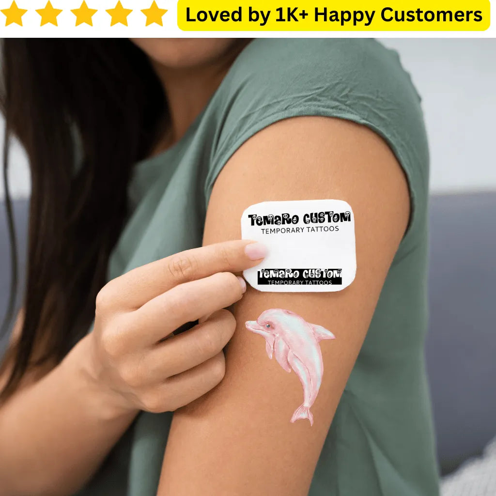 Person applying a pink dolphin temporary tattoo to their arm, with 'Tumaro Custom' branding visible. Expressive Tattoos for Ladies Back - Love Style Without the Commitment